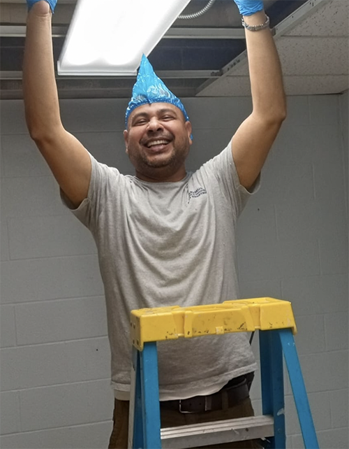 Custodial staff smiling while on a ladder