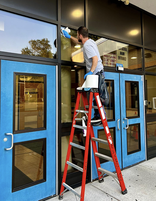 Custodial staff cleaning windows on a ladder