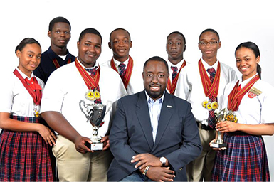 Group of students wearing red ribbons and holding trophies around a man dressed in a suit